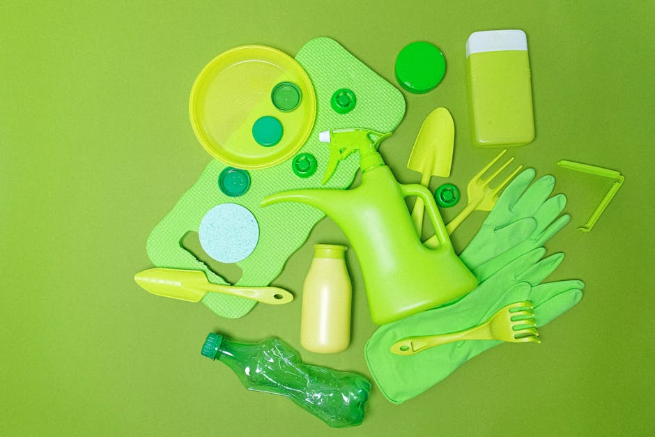 A collection of gardening tools and supplies arranged on a vibrant green background, highlighting gardening activities relevant to lawn and garden maintenance. The assortment includes a bright green watering can with a long spout, a small yellow hand trowel, and a matching fork, all designed for planting and soil aeration. Surrounding these are green latex gloves, a yellow plastic rake, and a yellow-handled garden knife, suitable for trimming and transplanting. There are also several small containers and caps, likely for plant fertilizers or chemicals, arranged next to a green rectangular sponge and a clear plastic water bottle, emphasizing garden care tools. The layout suggests recent or upcoming outdoor gardening work, with a focus on landscaping, hedge trimming, and lawn care, reflecting the comprehensive garden maintenance activities discussed on the page, 'Brent council garden waste rules every gardener must know.' This visually accurate description aims to assist visually impaired users and aligns with the themes of outdoor garden upkeep facilitated by Gardeners Brent.